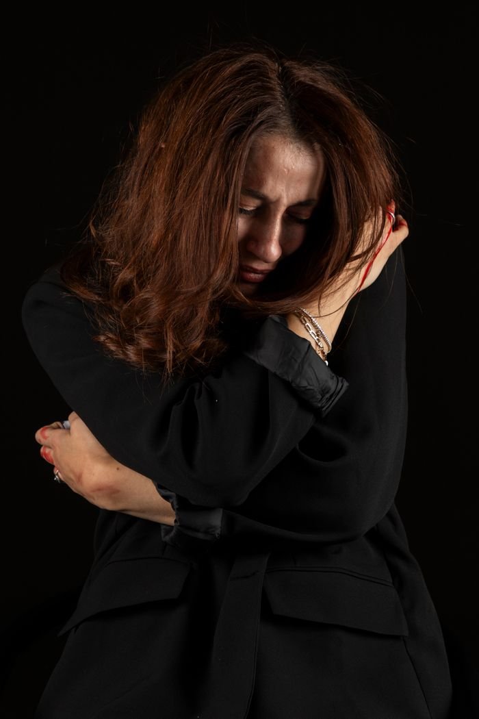 Emotional portrait of a woman hugging herself in a dark room, conveying sadness.